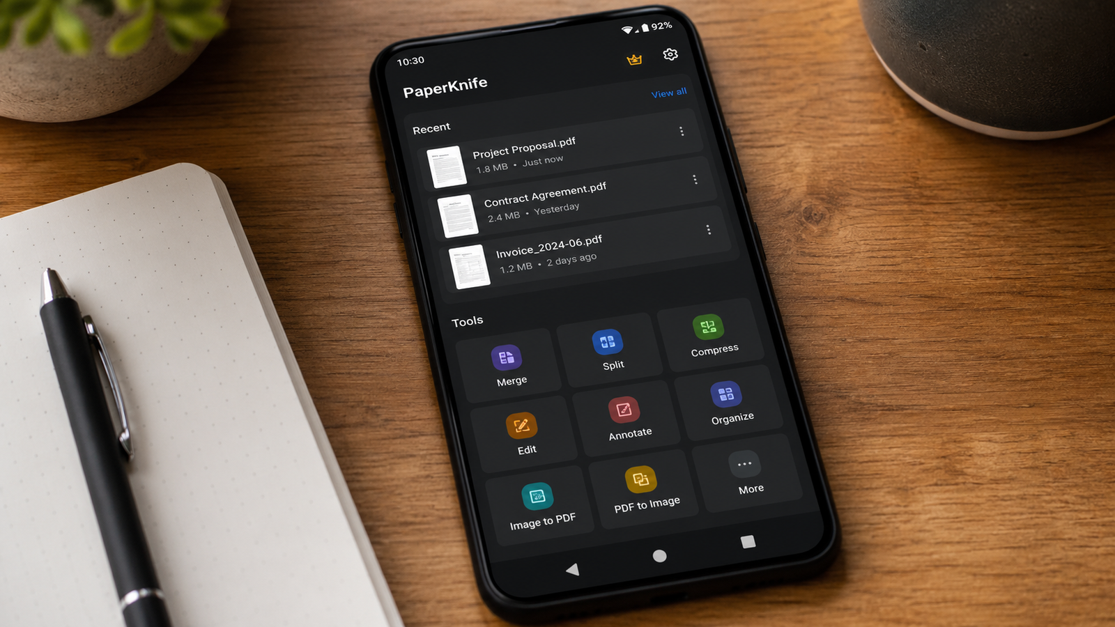 Imagem ilustrativa: Aplicativo PaperKnife aberto em um smartphone sobre mesa com caderno e caneta
